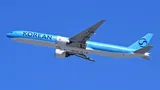 Korean Air Boeing 777-300ER climbing away from Boston Logan Airport in three-quarter view against a clear sky, showing its long stretched body and swept-to-a-point wingtips.