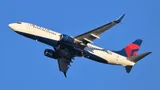 Delta Air Lines Boeing 737-800 climbing out of Boston against a clear blue sky, three-quarter view filling the frame and showing its flattened CFM56 engine pods and blended wingtip blades.