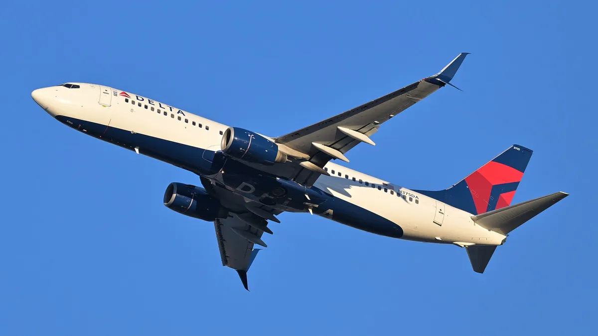 Delta Air Lines Boeing 737-800 climbing out of Boston against a clear blue sky, three-quarter view filling the frame and showing its flattened CFM56 engine pods and blended wingtip blades.
