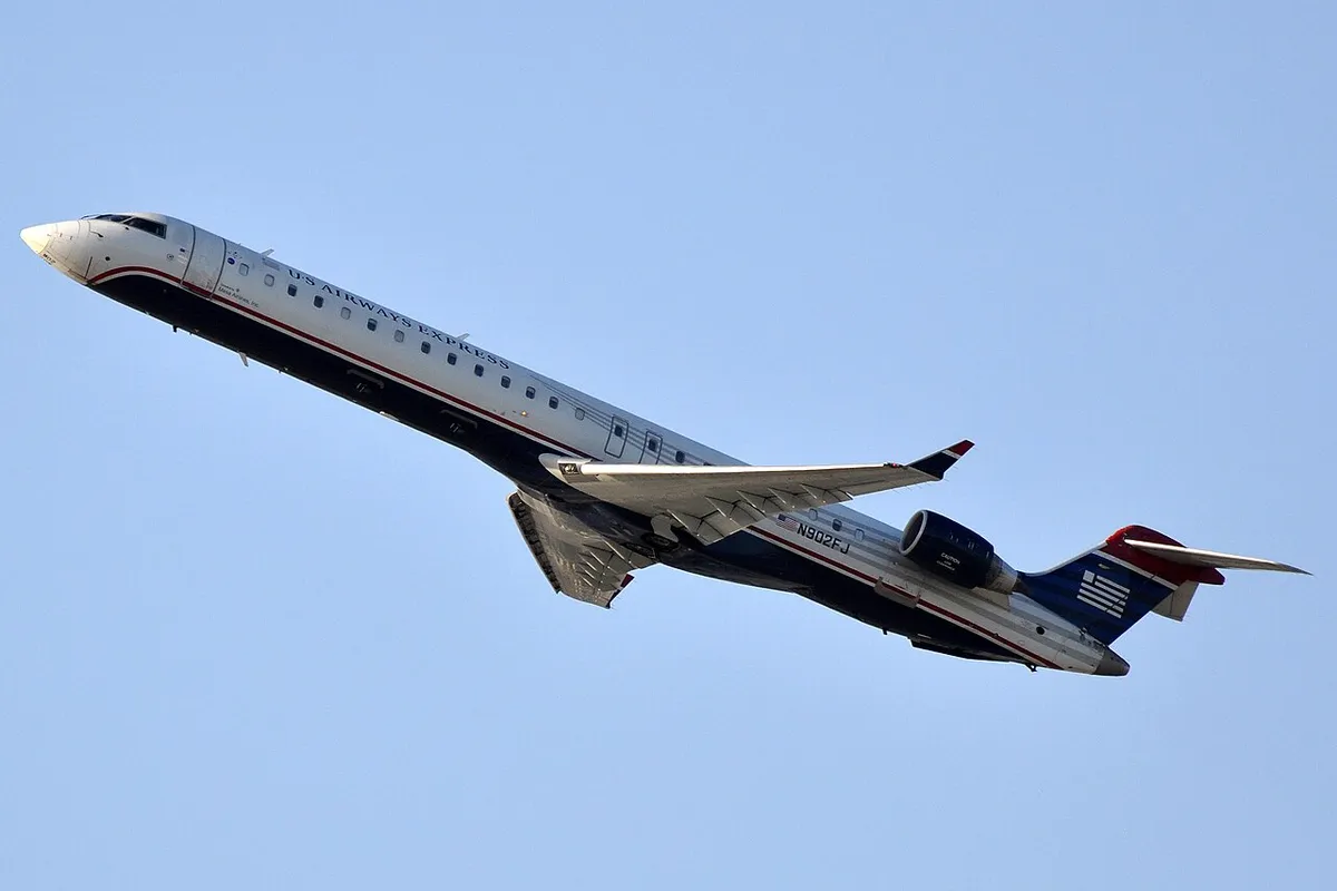 Mesa Airlines CRJ900 climbing away in US Airways Express livery, three-quarter view showing its upturned wingtip blades and stretched body.