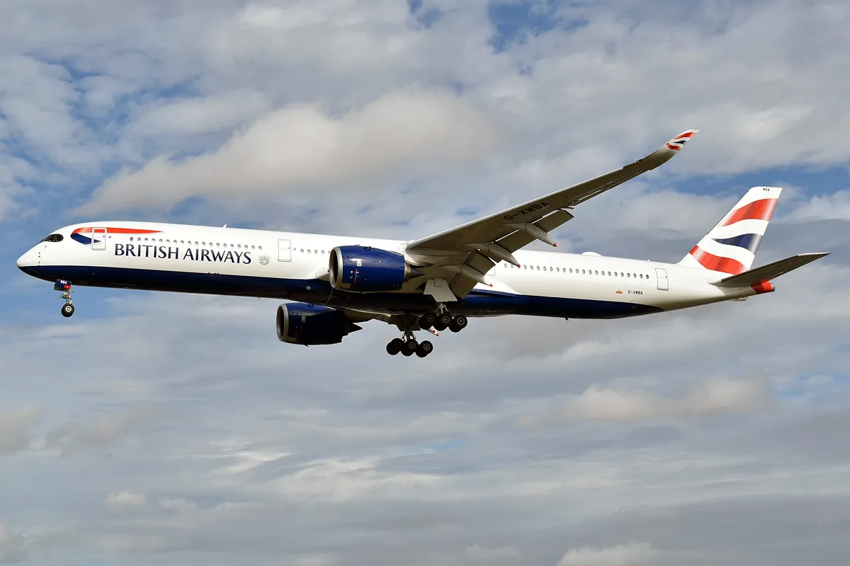 British Airways Airbus A350-1000 on final approach, three-quarter view showing its stretched body, raccoon-mask cockpit windows, and six-wheel main landing gear.