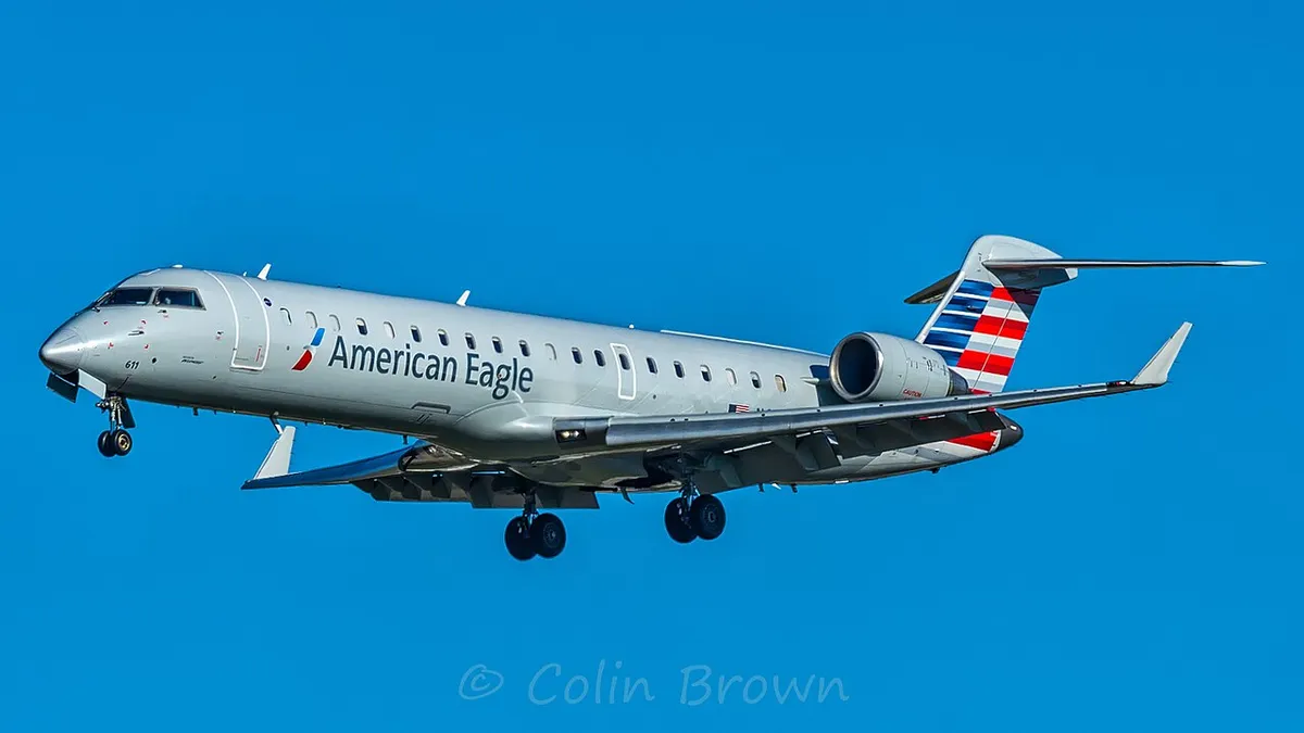American Eagle Embraer ERJ145LR climbing away against a blue sky, three-quarter view showing its slim body, rear-mounted engines, and T-tail.