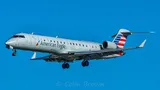 American Eagle Embraer ERJ145LR climbing away against a blue sky, three-quarter view showing its slim body, rear-mounted engines, and T-tail.