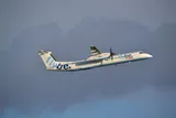 Flybe Dash 8 Q400 climbing away in side profile, showing its high wing, T-tail, and twin six-blade turboprops against a stormy sky.