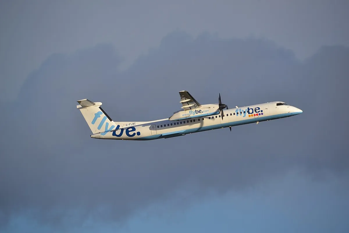Flybe Dash 8 Q400 climbing away in side profile, showing its high wing, T-tail, and twin six-blade turboprops against a stormy sky.