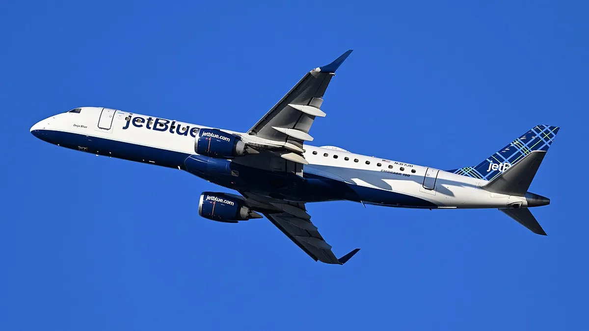 JetBlue Embraer E190 climbing away against a blue sky, three-quarter view showing its underwing engines, upturned wingtip blades, and boxy notched cockpit windows.