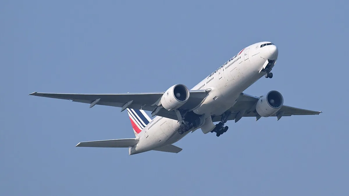 Air France Boeing 777-200ER climbing away from Boston Logan Airport in three-quarter view against a clear sky, showing its plain wingtips and six-wheel main landing gear.