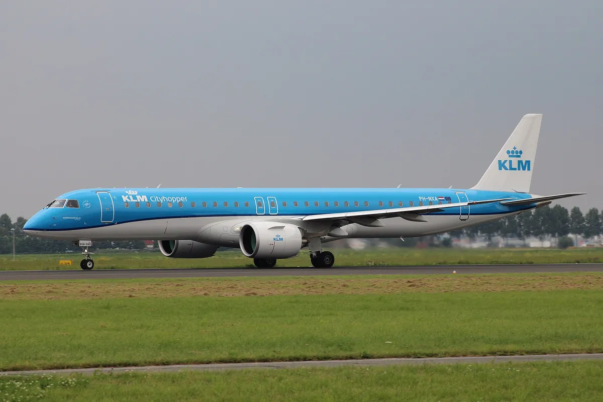 KLM Cityhopper Embraer E195-E2 PH-NXA in side profile on the runway, showing the swept pointed wingtips and the oversized Pratt & Whitney PW1900G engine pods.