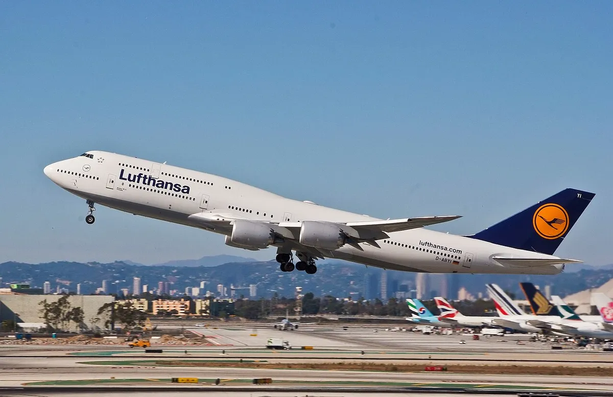 Lufthansa Boeing 747-8 climbing away from Los Angeles International Airport in side profile, showing its swept-to-a-point raked wingtip and extended forward hump.