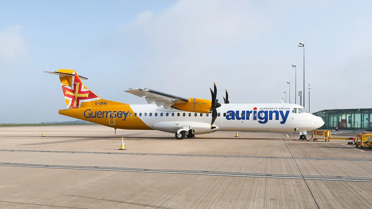 Aurigny Air Services ATR 72-600 parked on the apron in side profile against a clear sky, showing its high-mounted wing and twin turboprop engines.