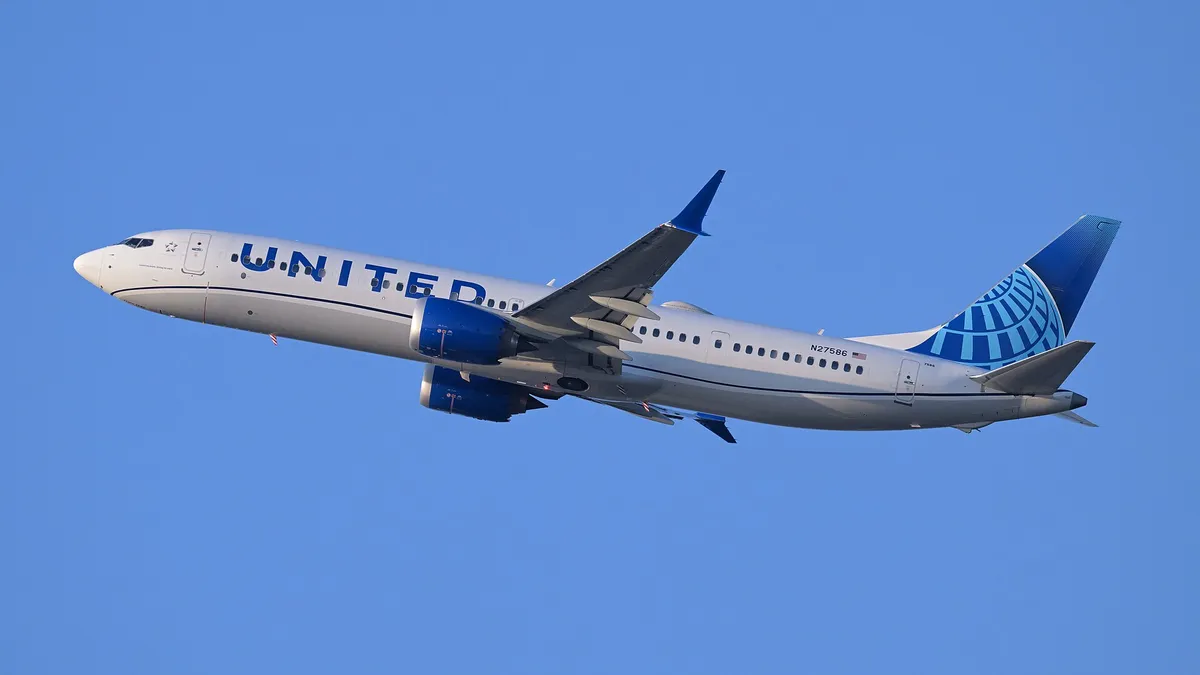 United Airlines Boeing 737 MAX 9 climbing out of Boston against a clear blue sky, three-quarter view filling the frame and showing its oversized LEAP-1B engine pods and split-blade wingtips.
