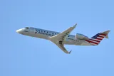 SkyWest Airlines CRJ200 climbing away in American Eagle livery, three-quarter view showing its plain wingtips and stubby, tightly coupled body.