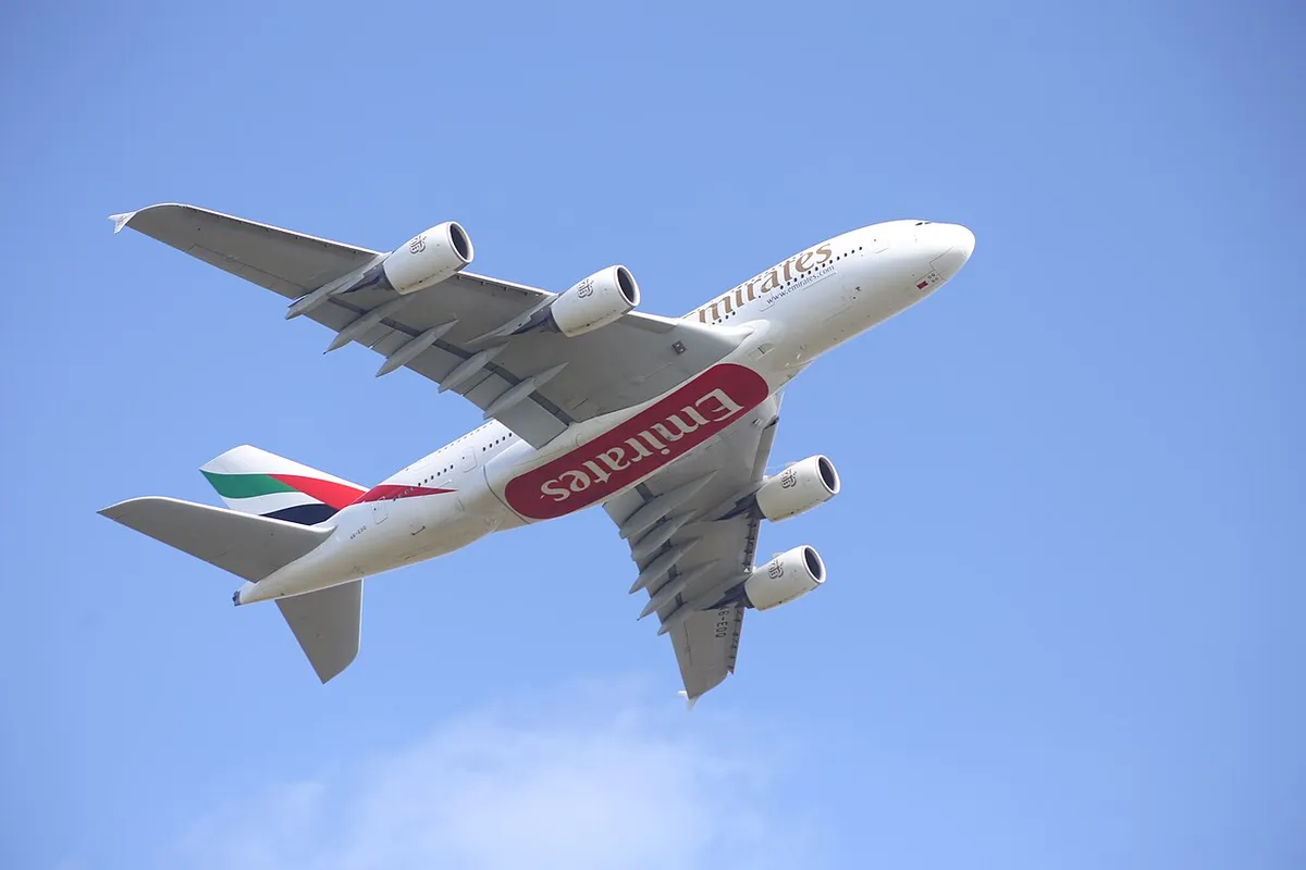 Emirates Airbus A380-861 banking directly overhead after takeoff, showing the underside outline with all four engines, the full wingspan, and the double-deck body cross-section against a clear sky.