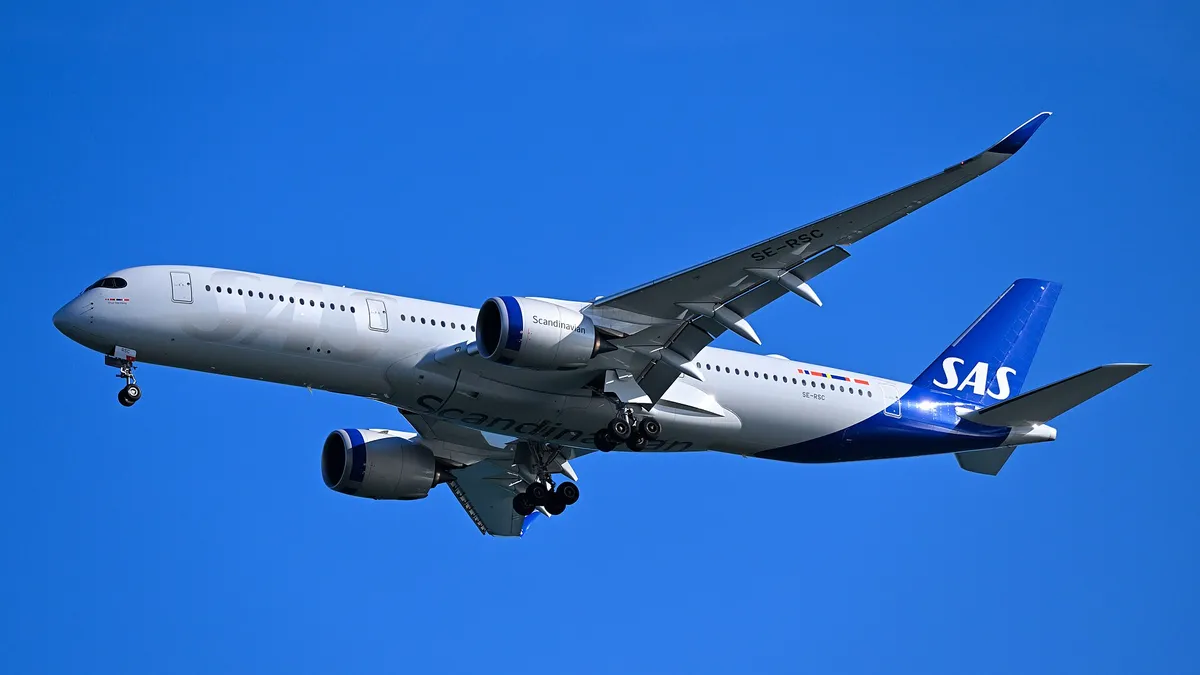 SAS Airbus A350-900 seen from below-quarter on final approach, showing the belly, smooth-rimmed engine pods, and four-wheel main landing gear.