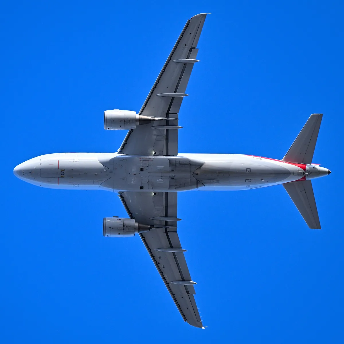 American Airlines Airbus A319-112 seen directly from below against a clear blue sky, showing the compact underside outline and flat wingtip fences.