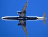 Delta Air Lines Airbus A321-211 seen directly from below against a clear blue sky, showing the stretched underside outline and slim, round ceo-generation engine pods.