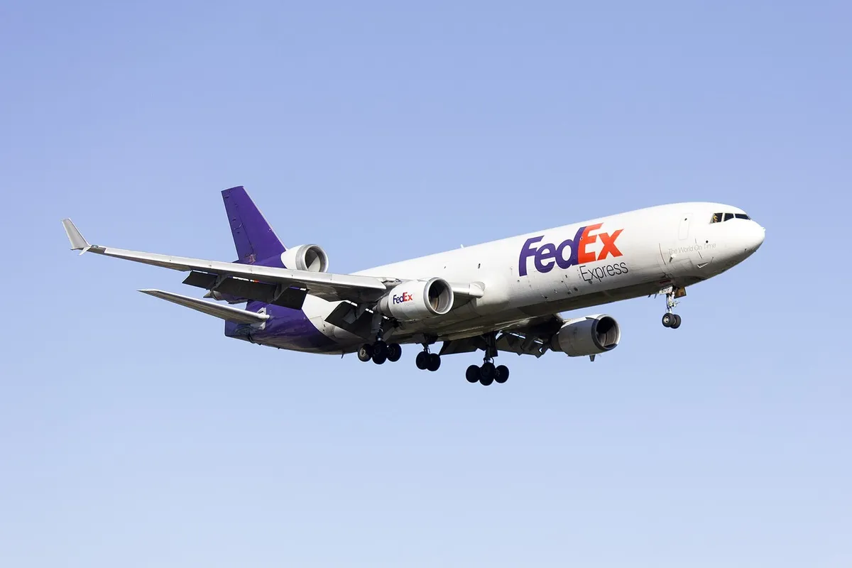 FedEx Express McDonnell Douglas MD-11F N609FE on final approach with gear down against a clear blue sky, seen from a below-quarter angle showing the underside of the wings and the trijet tail engine.