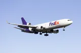 FedEx Express McDonnell Douglas MD-11F N609FE on final approach with gear down against a clear blue sky, seen from a below-quarter angle showing the underside of the wings and the trijet tail engine.