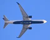 Delta Air Lines Boeing 767-300ER seen directly from below departing Boston, showing the underside outline and wide body cross-section.