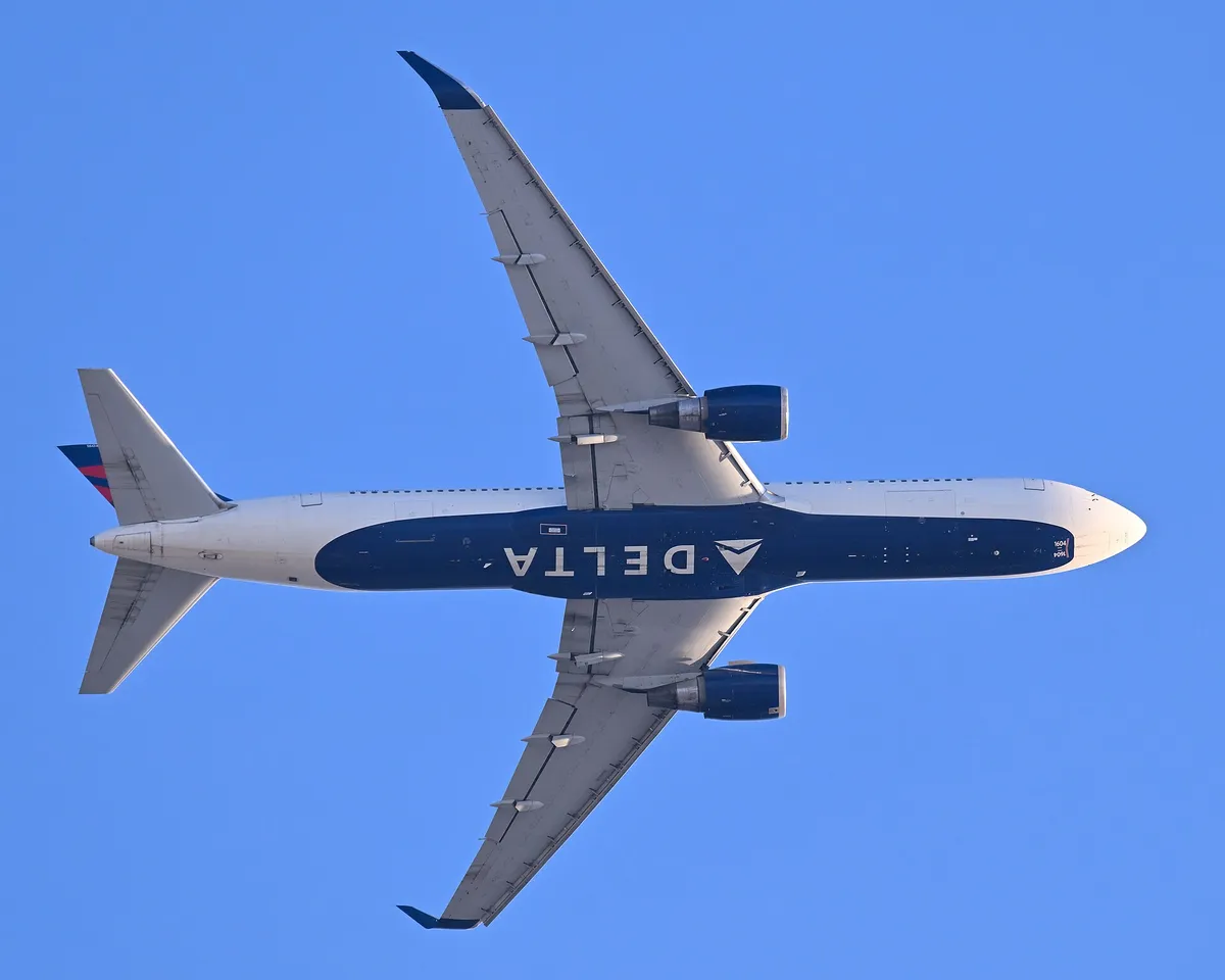 Delta Air Lines Boeing 767-300ER seen directly from below departing Boston, showing the underside outline and wide body cross-section.