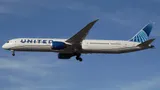 United Airlines Boeing 787-10 N13013 on final approach with gear down, seen from a below-quarter angle against a clear sky, showing the underside of the wings and long body.