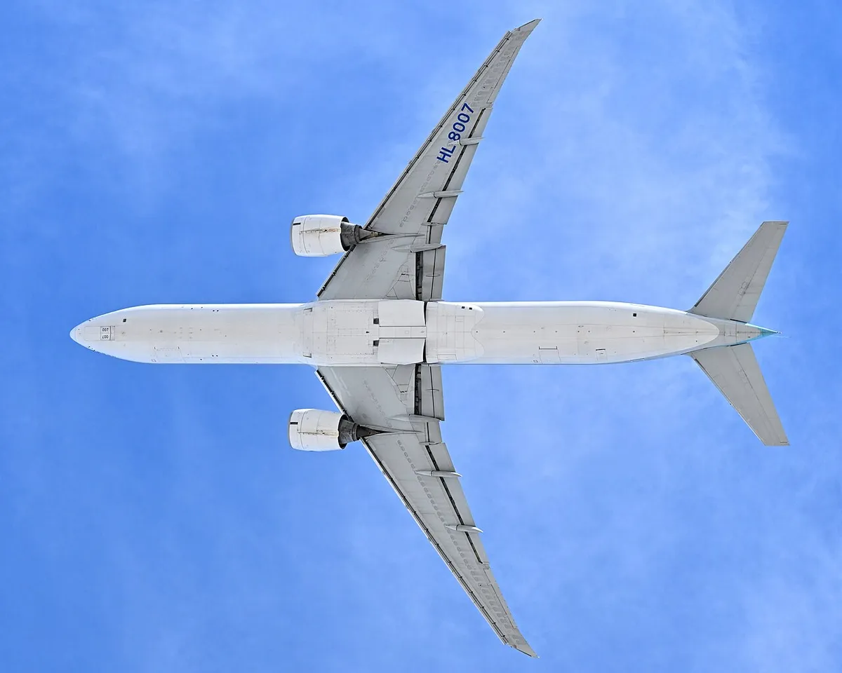 Korean Air Boeing 777-300ER seen directly from below climbing overhead, showing the full underside outline, long tail cone, and paired underwing engines against a clear sky.