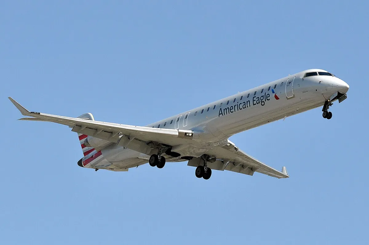 American Eagle CRJ900 seen from below on final approach, gear down, showing the upturned wingtip blades and rear-mounted engines.
