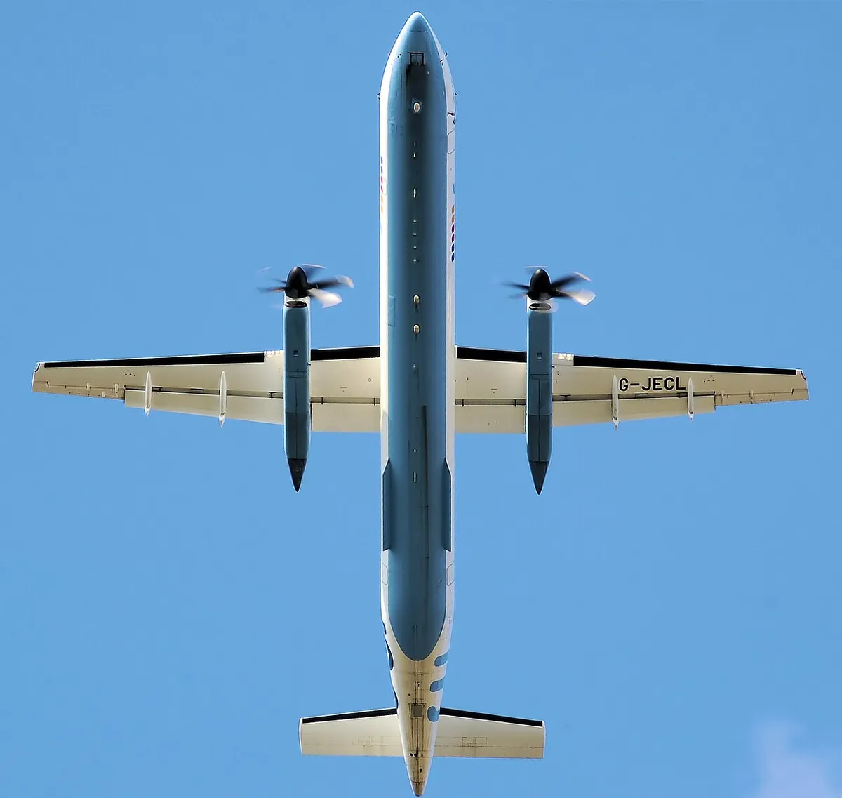 Flybe Dash 8 Q400 seen directly from below on takeoff, showing the high wing, twin propellers, and stretched body.