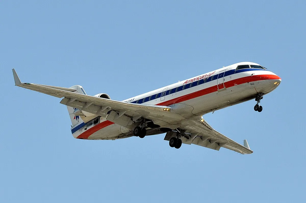 American Eagle CRJ200 seen from below on final approach, gear down, showing the plain wingtips and rear-mounted engines.